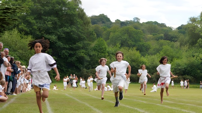 Schüler der Edinburgh Steiner School laufen in weißen Kleidern über ein grünes Feld umgeben von Bäumen.
