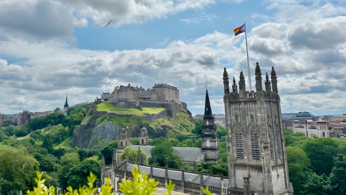 Ein grüner Hügel mit mittelalterlicher Burg und hoher Kathedrale vor wolkigem Himmel nahe der Edinburgh Steiner School.