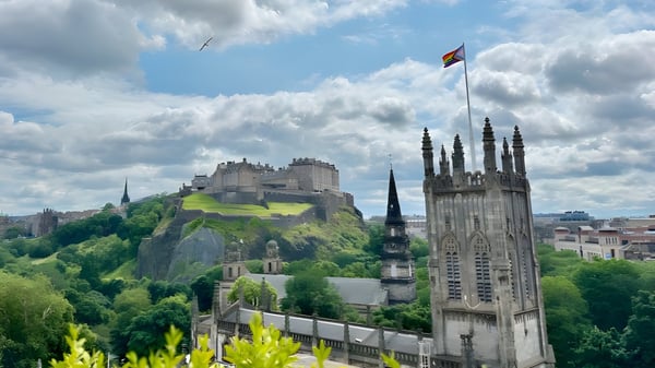 Das Edinburgh Steiner School Gebäude befindet sich auf einem felsigen Hügel mit einer Kathedrale im Hintergrund und einer Flagge im Himmel.