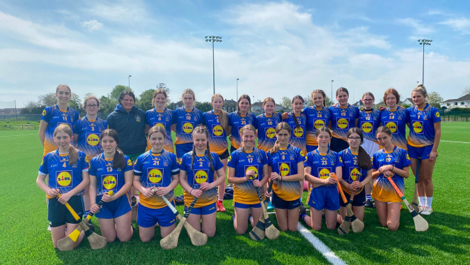 Eine Gruppe junger Athletinnen in blauen und gelben Uniformen posiert auf dem Sportfeld des Edmund Rice College.