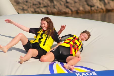 Zwei Schülerinnen des Edmund Rice College sitzen in Rettungswesten auf einem weißen Schlauchboot vor Schilf.