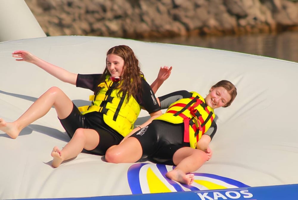 Zwei Schülerinnen des Edmund Rice College sitzen in Rettungswesten auf einem weißen Schlauchboot vor Schilf.