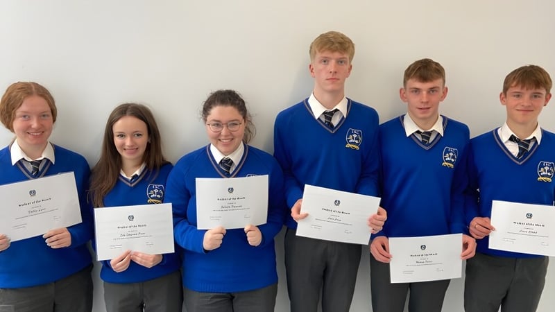 Schüler des Edmund Rice College in Schuluniformen halten Zertifikate vor einem weißen Hintergrund.