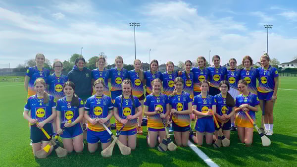 Eine Gruppe weiblicher Athletinnen posiert auf dem Sportfeld des Edmund Rice College mit Stadionlichtern im Hintergrund.