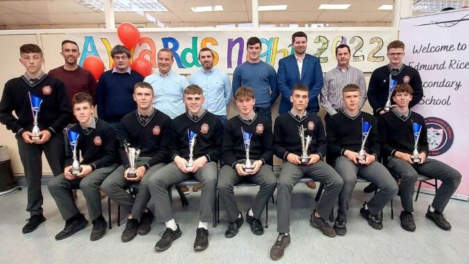 Eine Gruppe von Schülern steht und sitzt vor einem bunten Willkommensschild auf dem Campus der Edmund Rice Secondary School.