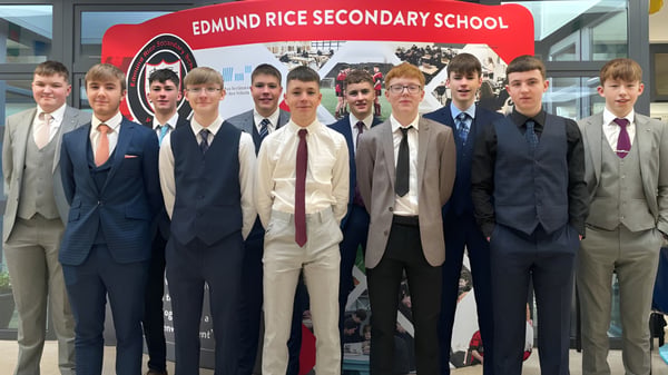 Eine Gruppe von Schülern steht in formeller Kleidung vor einem Schild der Edmund Rice Secondary School.