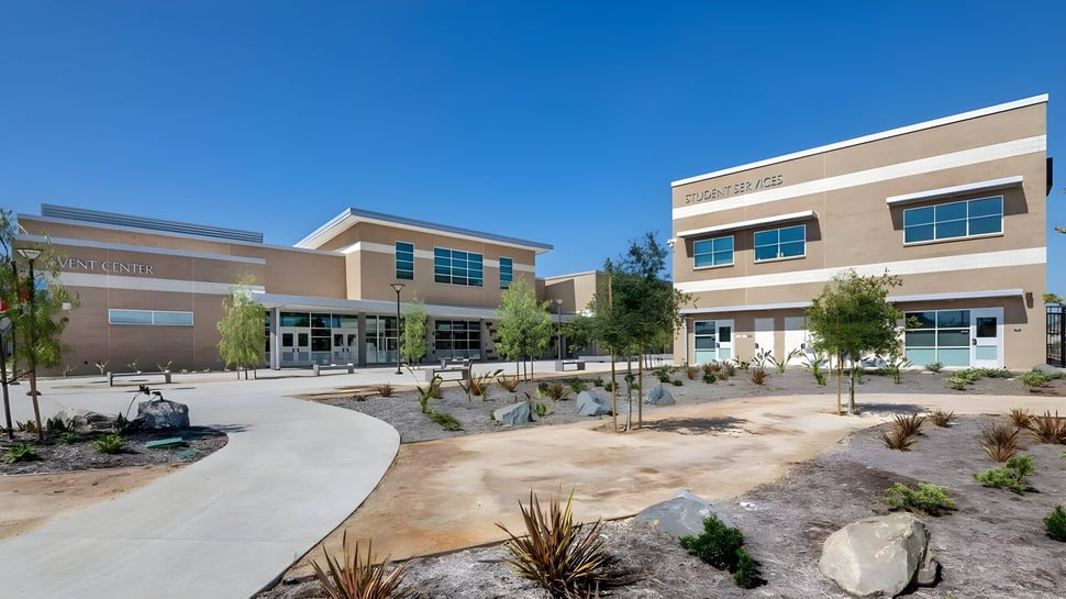 Das moderne mehrstöckige Gebäude der El Cajon Valley High School mit einem begrünten Innenhof und Weg bei klarem Himmel.