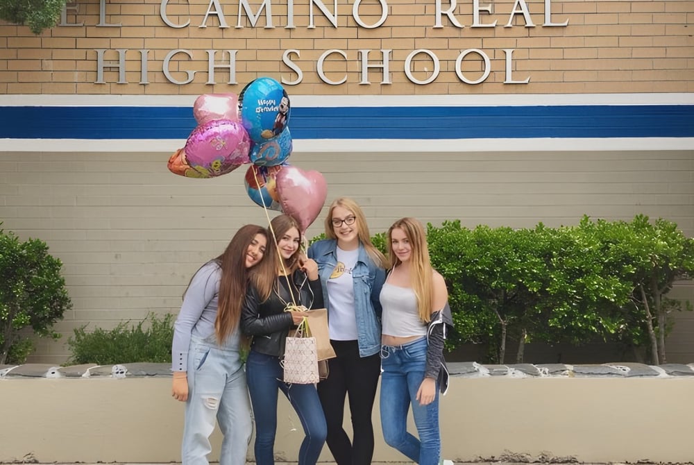 Vier Schülerinnen stehen vor dem Gebäude der El Camino Real Charter High School und halten bunte Luftballons.