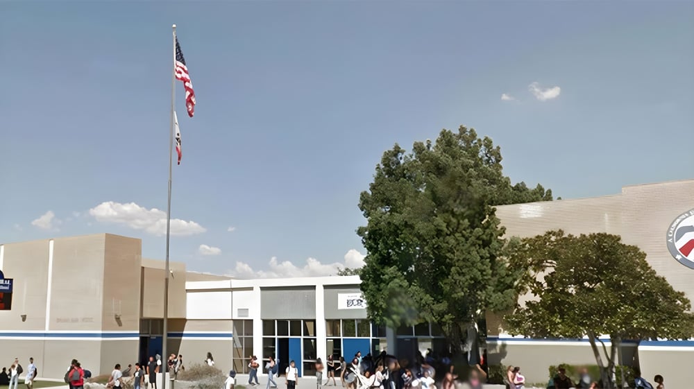 Die amerikanische Flagge weht über dem mehrstöckigen Gebäude der El Camino Real Charter High School mit Bäumen und Menschen im Vordergrund.