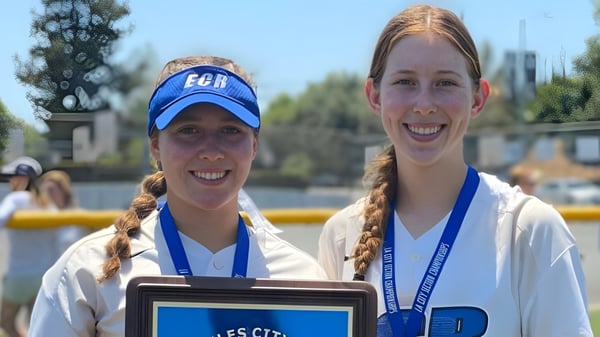 Zwei lächelnde Schülerinnen der El Camino Real Charter High School stehen vor einem Gewässer mit Bäumen und Gebäuden im Hintergrund.