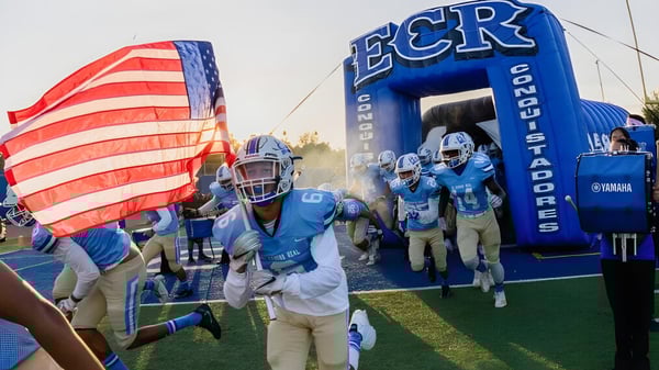 Die Fußballmannschaft der El Camino Real Charter High School läuft durch einen aufblasbaren Tunnel mit amerikanischer Flagge im Vordergrund.