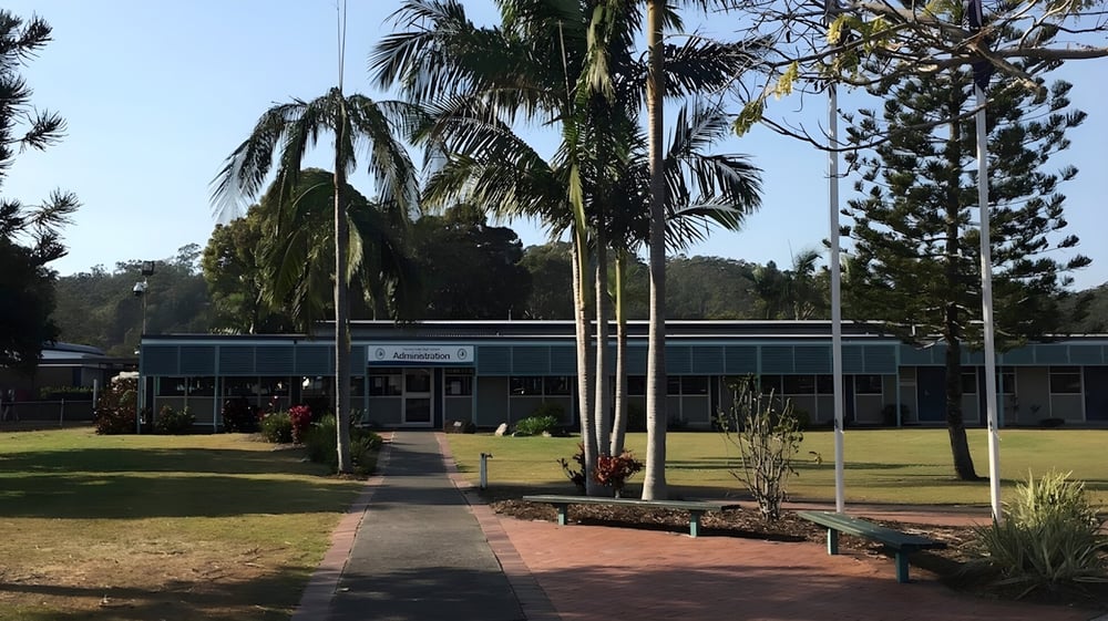 Das einstöckige Gebäude mit grünem Dach von Elanora State High School ist von Palmen und Grünflächen umgeben.