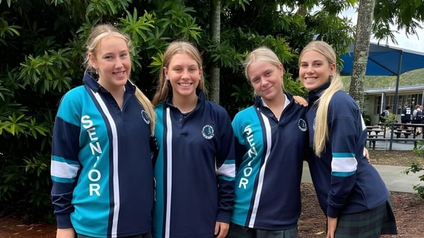 Vier Schülerinnen der Elanora State High School stehen im tropischen Außenbereich mit Palmen im Hintergrund.