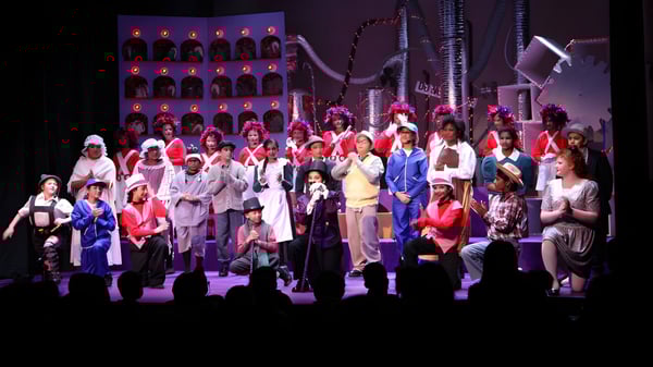 Eine große Gruppe von Schülerinnen und Schülern der Elgin Park Secondary School steht in farbenfrohen Kostümen auf der Bühne mit ausgeklügeltem Bühnenbild und Beleuchtung.