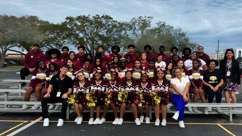 Eine Gruppe von Cheerleadern in weinroten Uniformen auf dem Sportplatz der Elite Preparatory Academy posiert zusammen.
