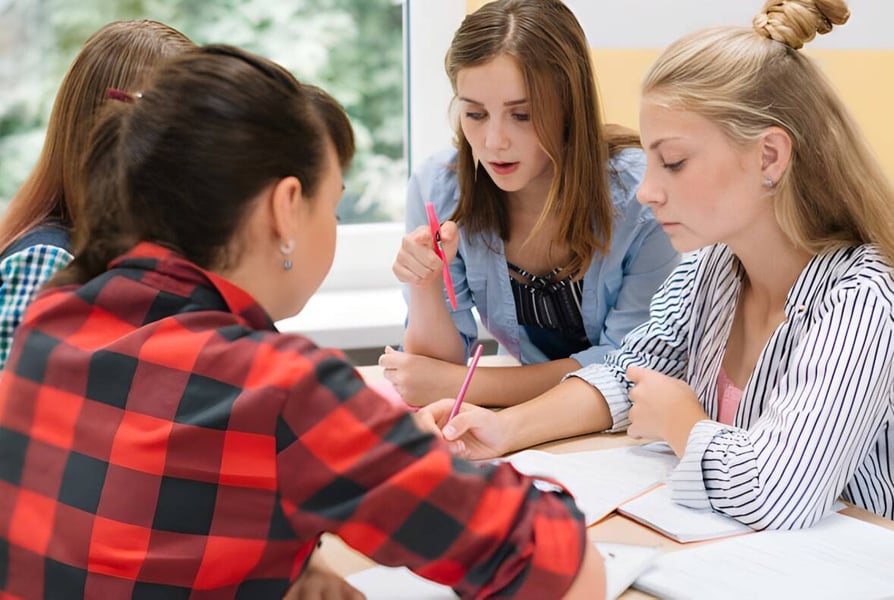 Vier Schülerinnen der Elite Preparatory Academy führen eine konzentrierte Diskussion in einem Innenraum.