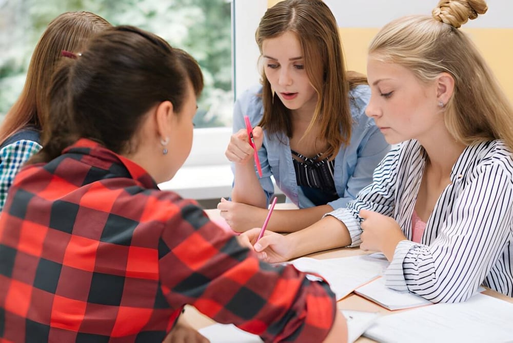 Vier Schülerinnen der Elite Preparatory Academy führen eine konzentrierte Diskussion in einem Innenraum.