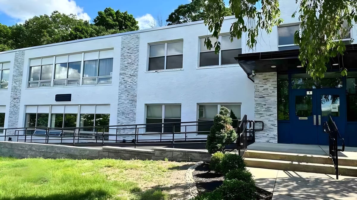 Das moderne mehrstöckige Gebäude der Elite Preparatory Academy ist von grünen Bäumen und einem Rasen umgeben.