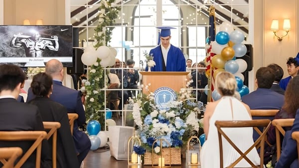 Ein Absolvent hält eine Rede bei der Abschlussfeier der Elite Preparatory Academy in einem festlich geschmückten Innenraum.