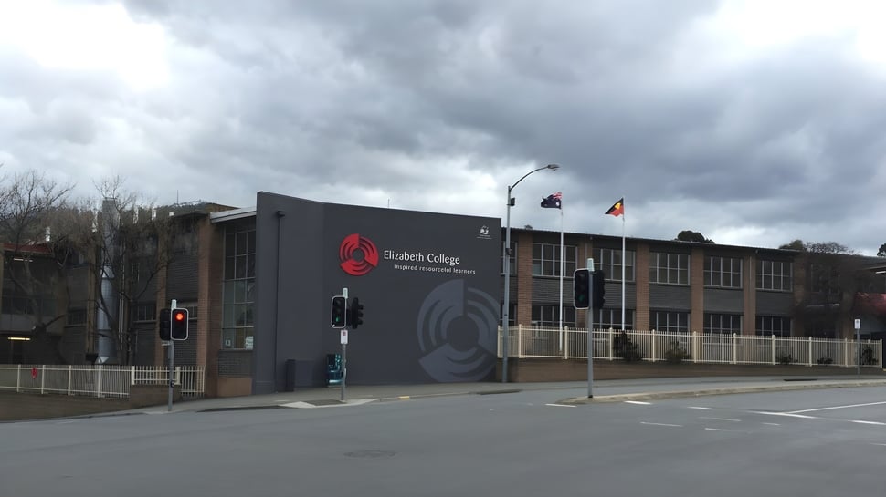 Das moderne Gebäude des Elizabeth College mit dem Logo an der Fassade unter einem bewölkten Himmel.