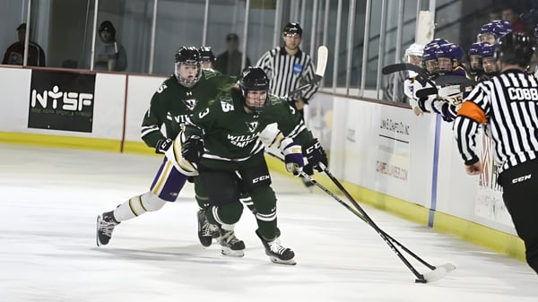 Schülerin trägt beim Hockeyspiel auf dem Eis den Puck und wird von Mitspielern sowie einem Schiedsrichter begleitet auf dem Campus der Elizabeth College.