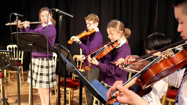 Eine Gruppe von Musikerinnen und Musikern in lila Outfits spielt auf der Bühne am Ellesmere College verschiedene Instrumente wie Geigen und Schlagzeug.