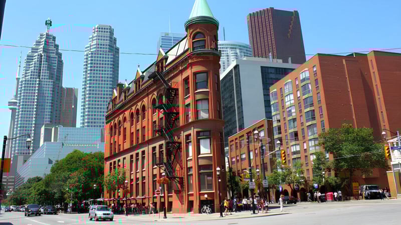 Das historische Backsteingebäude der Elmvale District High School steht vor modernen Wolkenkratzern in einer urbanen Umgebung.