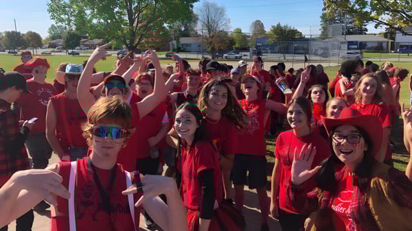 Eine Gruppe von Schülerinnen und Schülern der Elmvale District High School trägt rote T-Shirts und hebt jubelnd die Arme auf einem Feld.