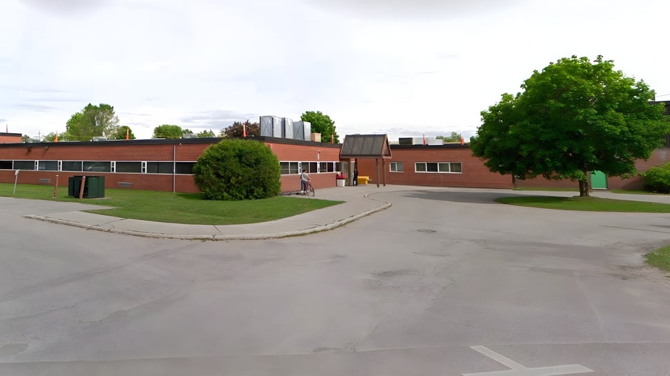 Das Backsteingebäude der Elmvale District High School mit Wiese und Bäumen im Vordergrund ist umgeben von einem gepflasterten Weg und weiteren Gebäuden im Hintergrund.