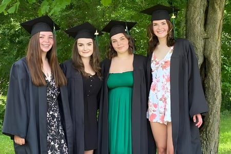 Vier Schülerinnen stehen in Abschlusskleidung im Grünen auf dem Gelände der Elmvale District High School.