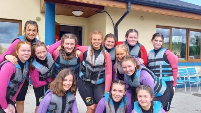Eine Gruppe junger Frauen in bunter Outdoor-Kleidung posiert vor einem Holzgebäude am Elphin Community College.