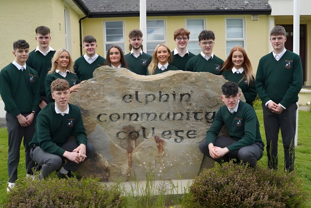 Eine Gruppe Schüler in Schuluniformen posiert vor dem großen Steinschild des Elphin Community College.