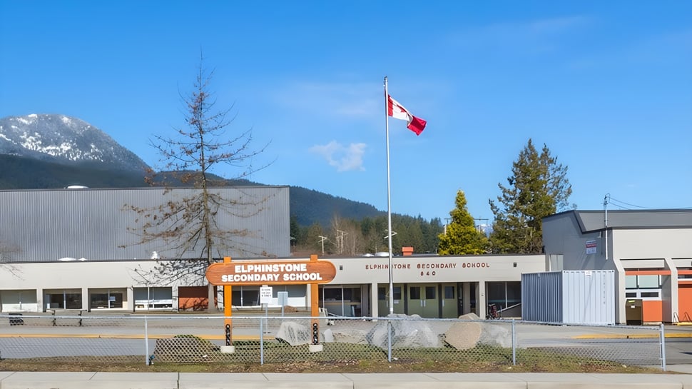 Das moderne Gebäude der Elphinstone Secondary School mit einer kanadischen Flagge und Bergen im Hintergrund.