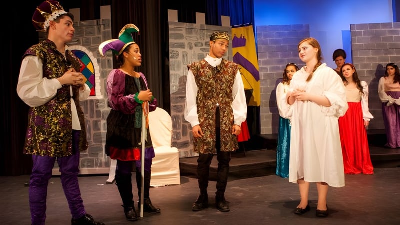 Schüler der Elphinstone Secondary School stehen in farbenfrohen Kostümen auf einer Bühne vor einer Steinmauer.