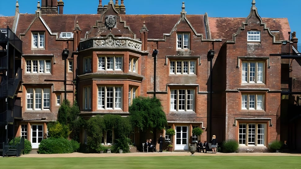 Das historische, verzierte Backsteingebäude auf dem Campus der Embley School ist von einem grünen Innenhof umgeben, in dem Schüler unterwegs sind.