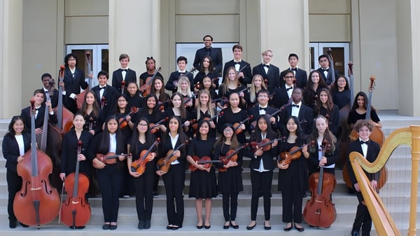 Eine große Gruppe Musiker in formeller Kleidung steht vor einem klassisch gestalteten Gebäude auf dem Campus der Embley.