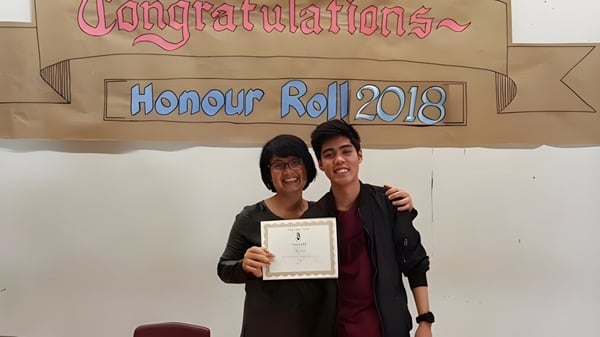 Zwei Personen halten gemeinsam ein Zertifikat vor einem Banner auf dem Campus der Emery Collegiate Institute.