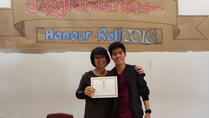 Zwei Personen halten gemeinsam ein Zertifikat vor einem Banner auf dem Campus der Emery Collegiate Institute.