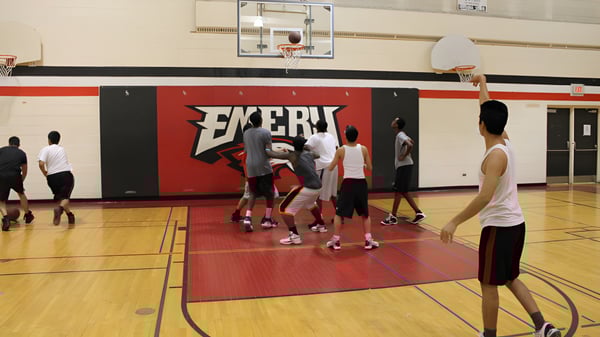 Eine Gruppe Schüler spielt Basketball auf dem Sportplatz des Emery Collegiate Institute vor einer großen Exert-Werbung.
