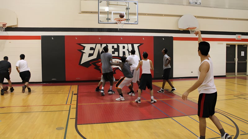 Eine Gruppe Schüler spielt Basketball auf dem Sportplatz des Emery Collegiate Institute vor einer großen Exert-Werbung.