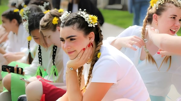 Eine Gruppe junger Frauen mit weißen Kleidern und Blumenkränzen steht auf einer Wiese auf dem Gelände der Emma Willard School.