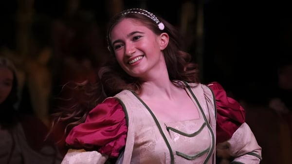 Eine Schülerin der Emma Willard School mit lockigem Haar und Perlenhaarbändern lächelt vor dunklem Hintergrund.