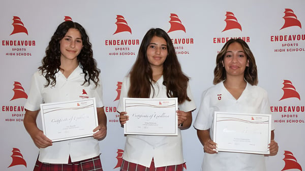 Drei Schülerinnen der Endeavour Sports High School halten vor einem Logo-Hintergrund ihre Zertifikate.