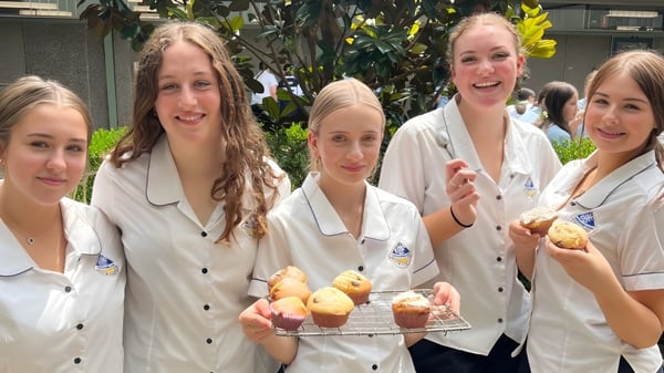 Schülerinnen der Engadine High School zeigen ein Tablett mit frisch gebackenen Backwaren vor grüner Kulisse.