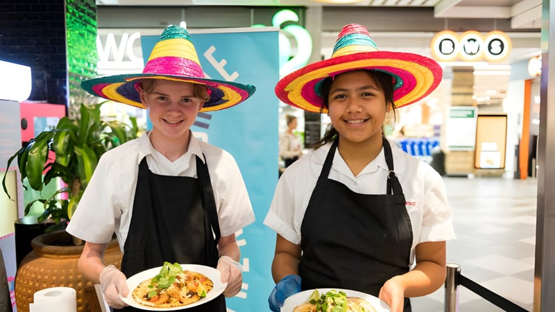 Zwei Personen tragen bunte Sombrero-Hüte und Schürzen in der Schulküche der Engadine High School.