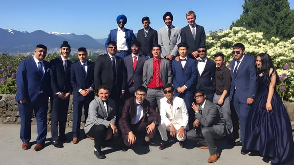 Eine Gruppe von Männern in formeller Kleidung posiert draußen mit Berglandschaft im Hintergrund auf dem Gelände der Enver Creek Secondary School.