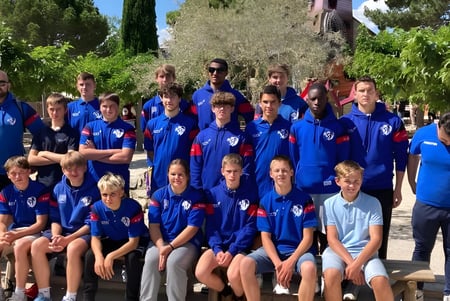 Eine Gruppe junger Athleten in blauen Uniformen posiert draußen umgeben von Bäumen auf dem Campus der Episcopal Sem' De Walbourg.