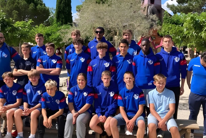 Eine Gruppe junger Athleten in blauen Uniformen posiert draußen umgeben von Bäumen auf dem Campus der Episcopal Sem' De Walbourg.