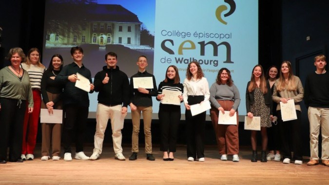 Schüler der Episcopal Sem' De Walbourg stehen auf einer Bühne und halten Urkunden bei einer Zeugnisübergabe.