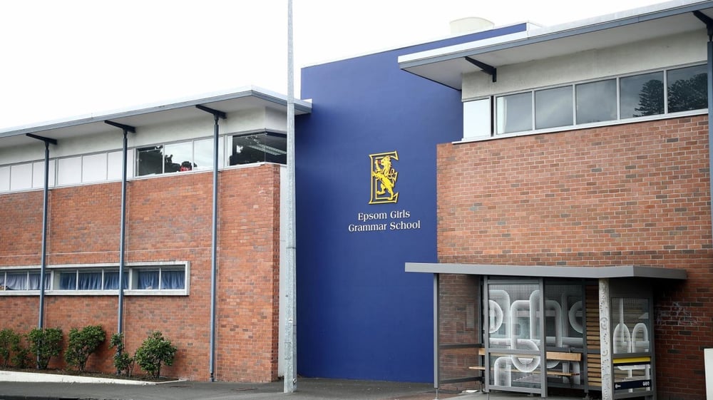 Das mehrstöckige Schulgebäude der Epsom Girls Grammar School mit blauer Fassade und einem Schild steht vor Grünflächen.